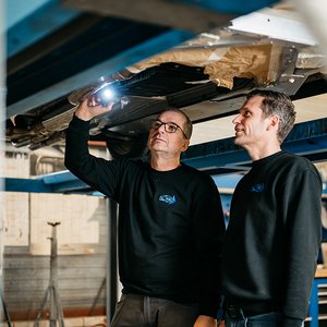Monteurs inspecteren de onderzijde van een auto met een lamp